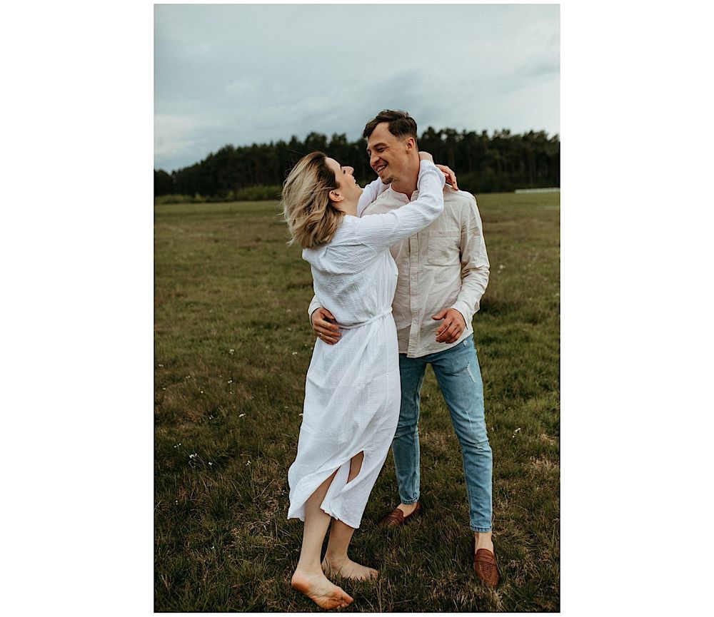 A couple in white clothing embracing in a rustic outdoor setting.