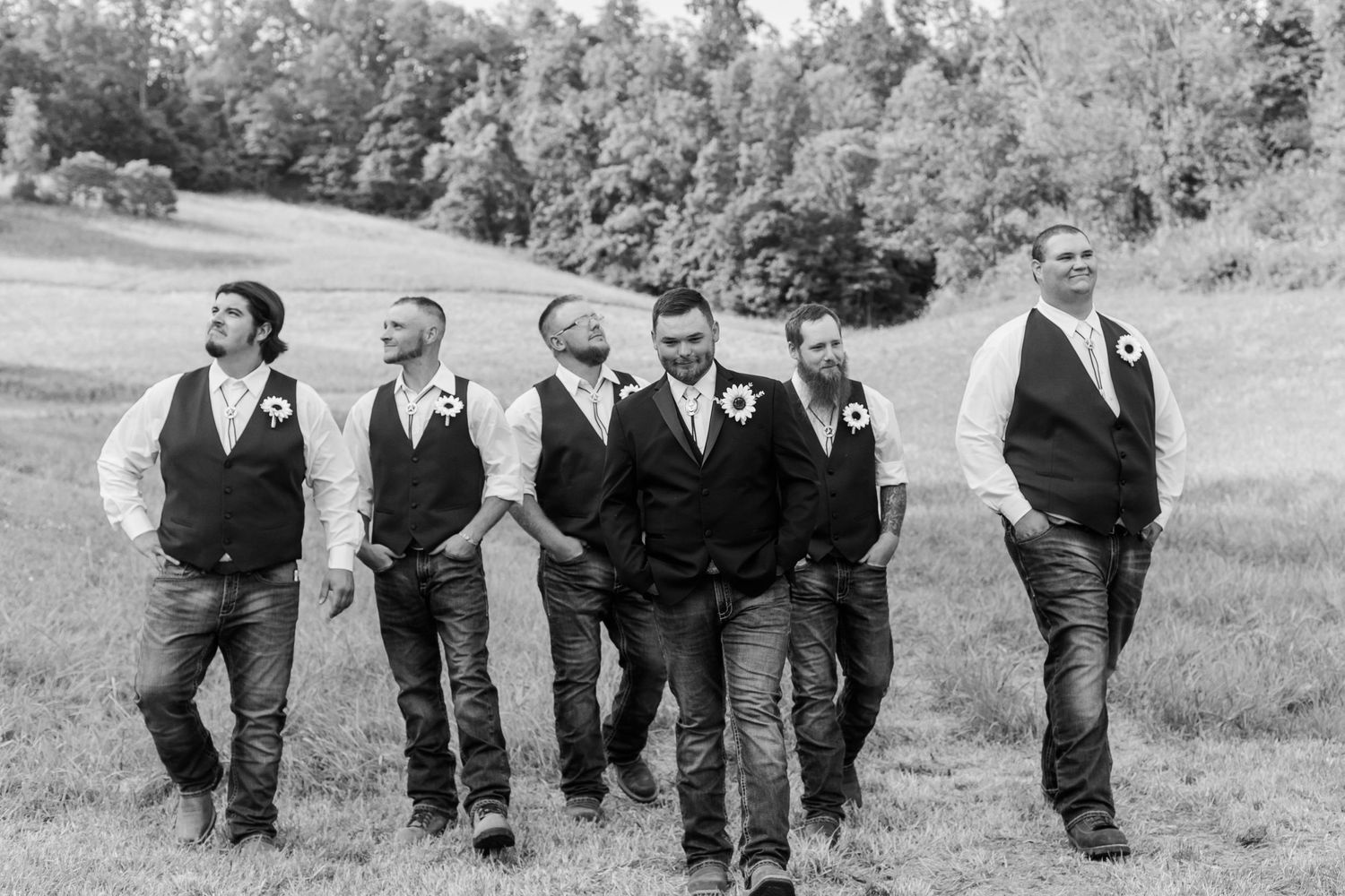 Wedding party walking and laughing together in black and white on a grassy field.