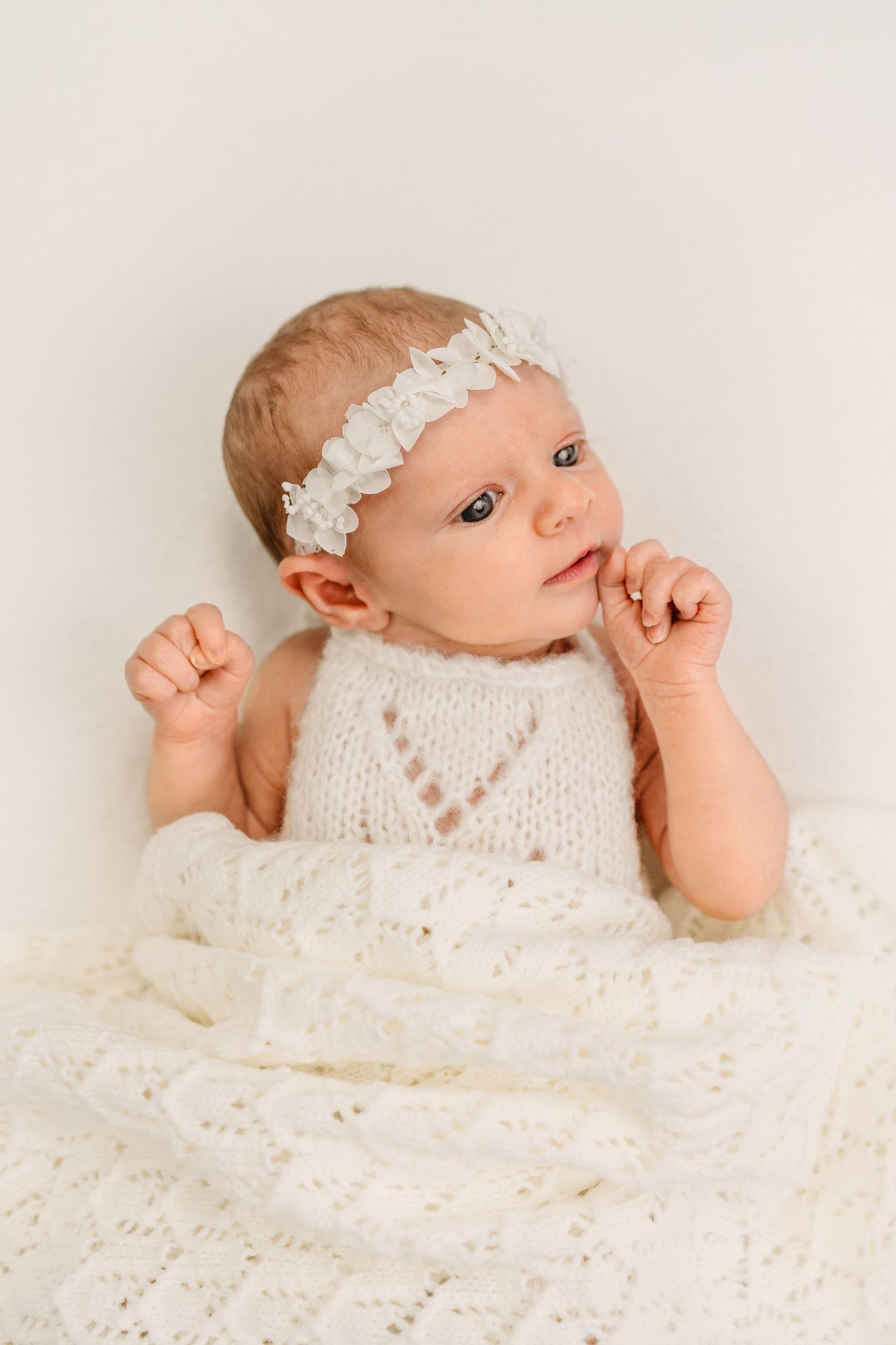 Baby wearing lace headband and knit outfit laying on white blanket.