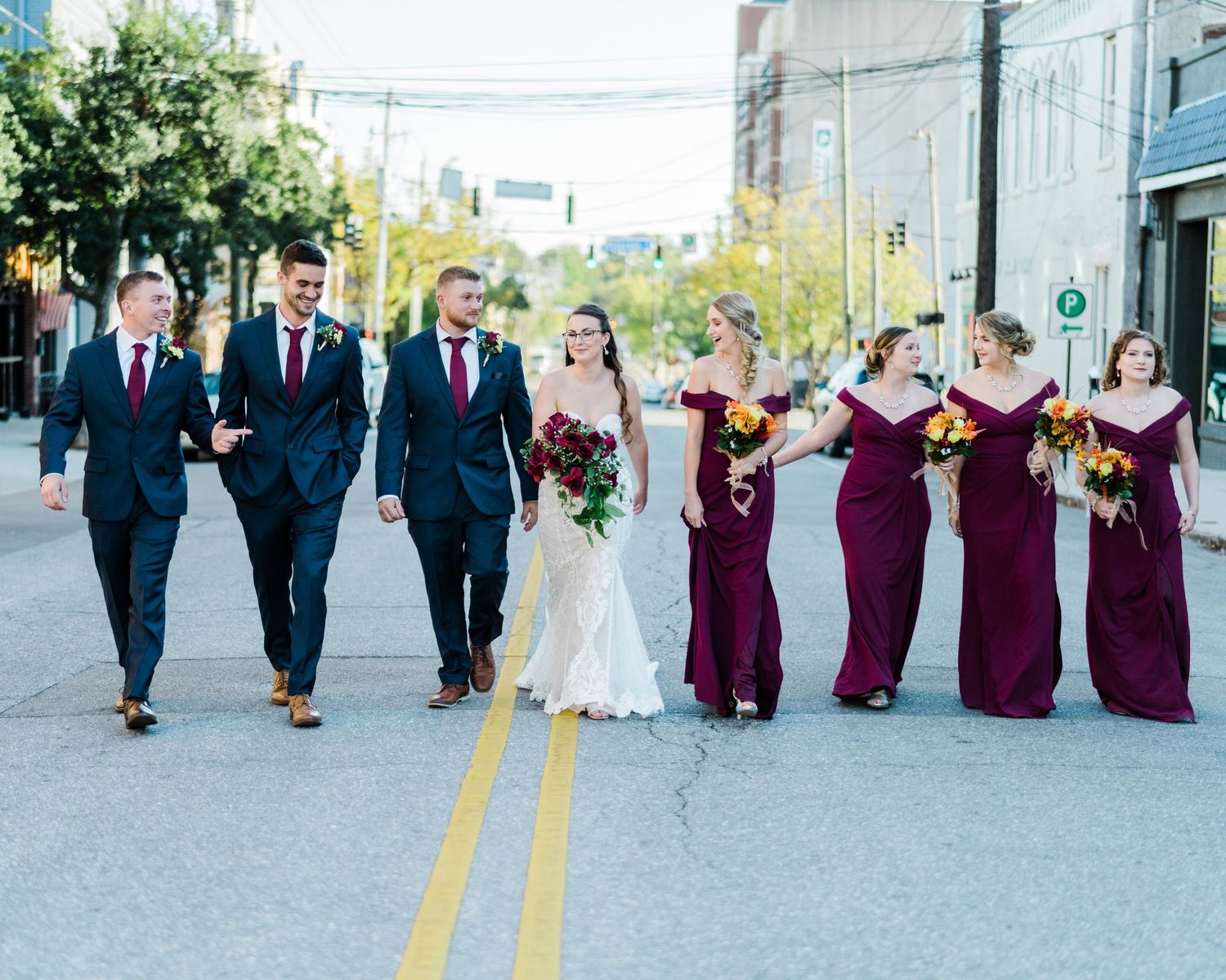 Wedding party in burgundy dresses and navy suits walking down city street during photo session.