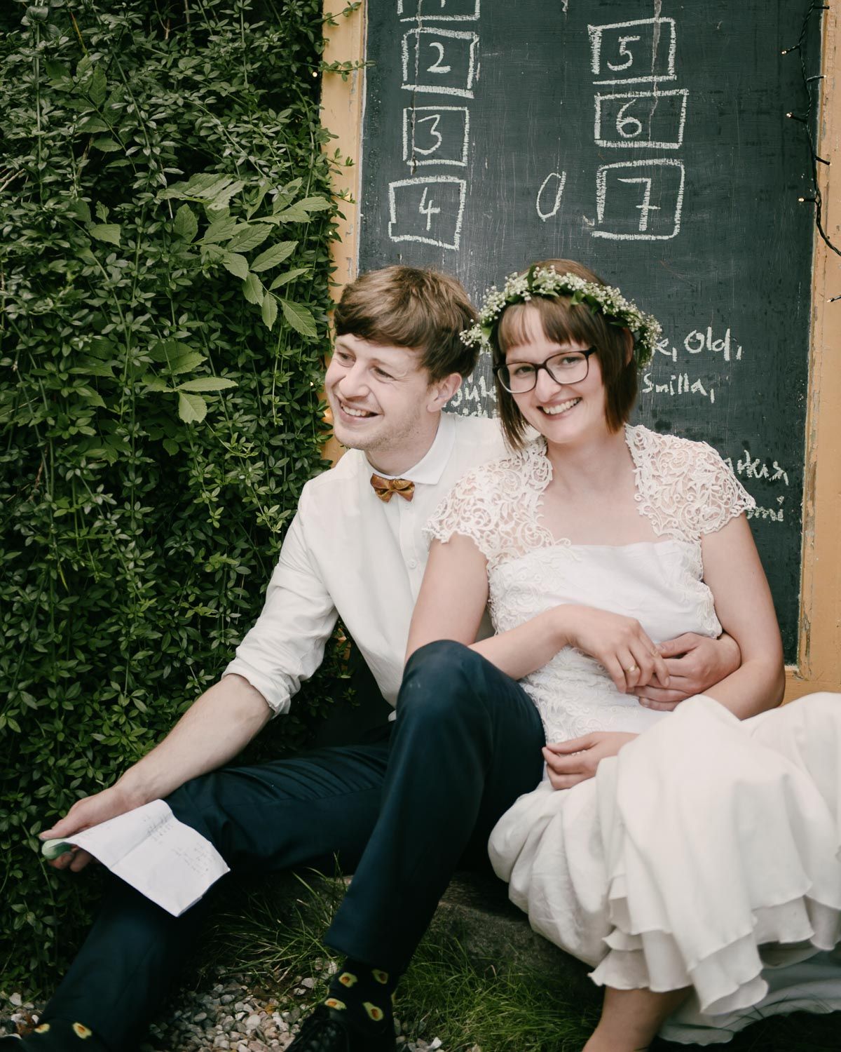 A couple sits together by a chalkboard at an outdoor wedding celebration.