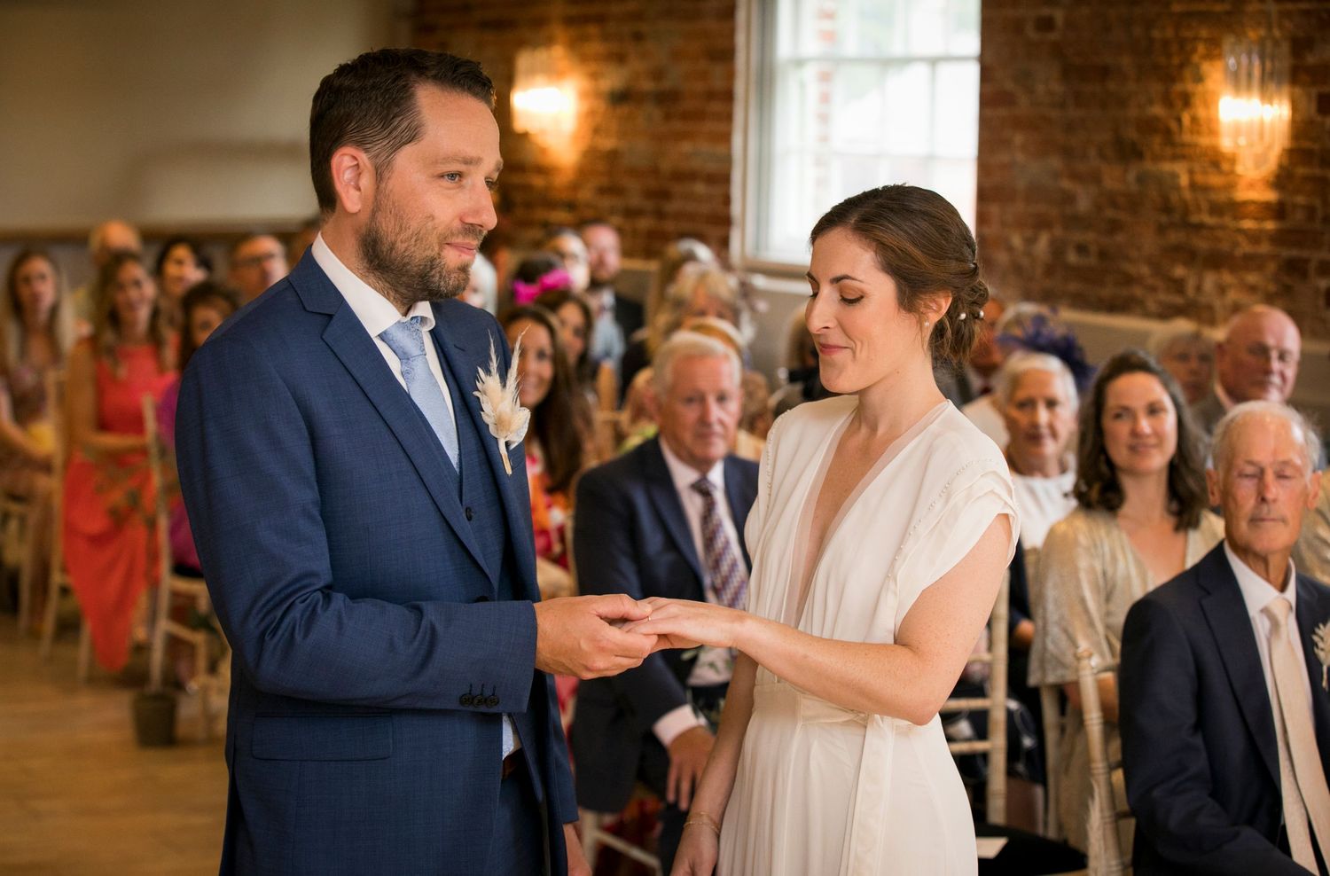 Couple exchanges rings during indoor wedding ceremony with exposed brick walls.
