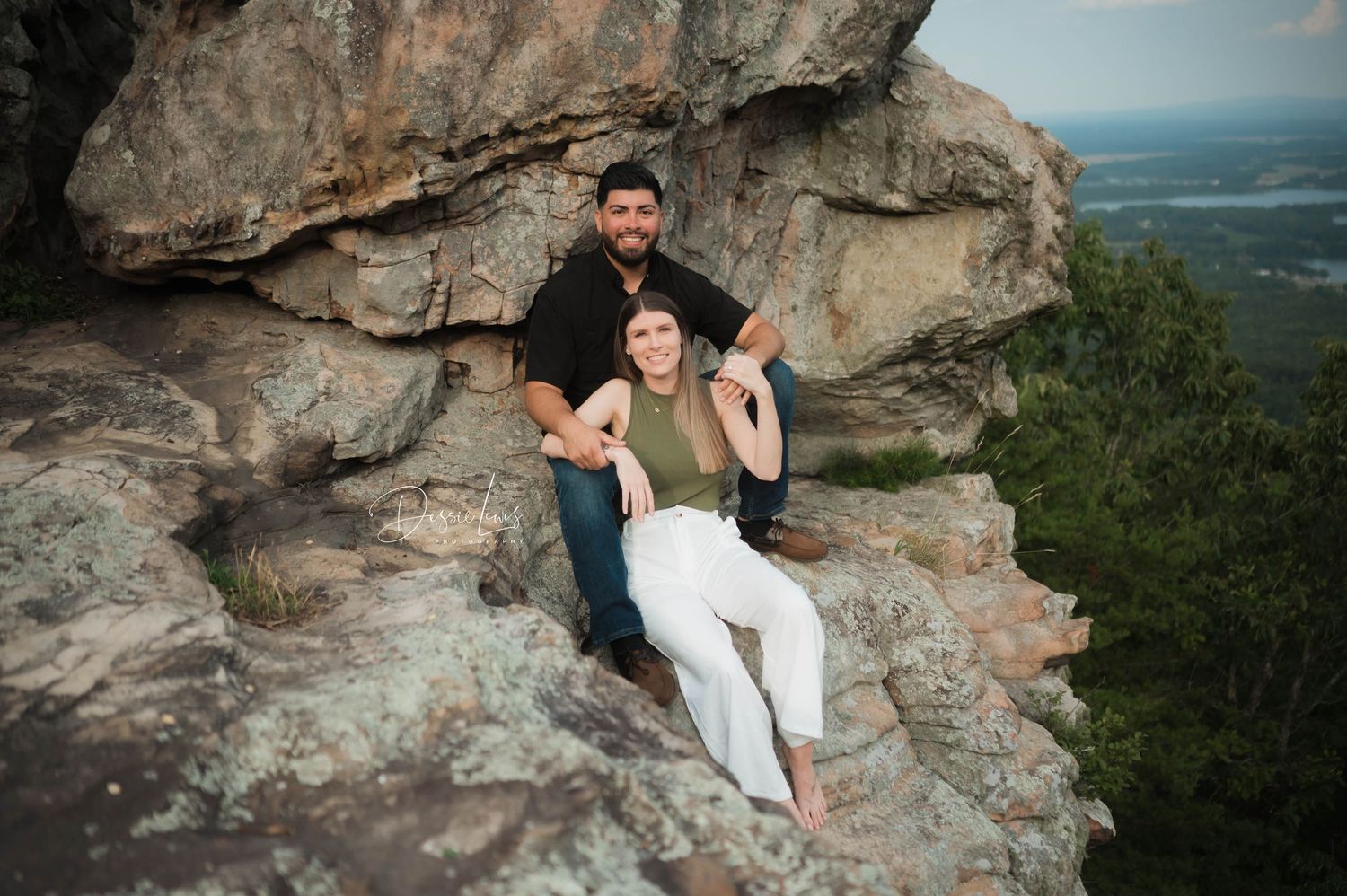 Couple sitting and embracing on rocky mountain overlook with scenic valley view.