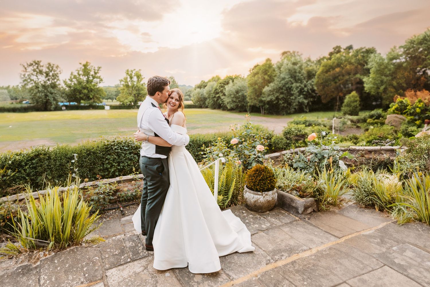 Incredible rose gold sunset with gorgeous young bride and groom smiling and embracing