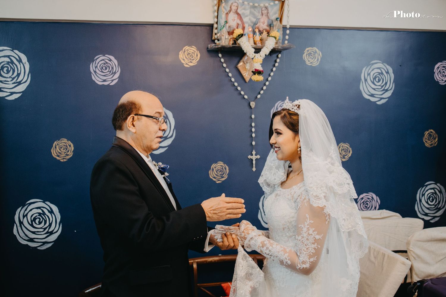 Wedding ceremony moment against blue wall with decorative white rose patterns.