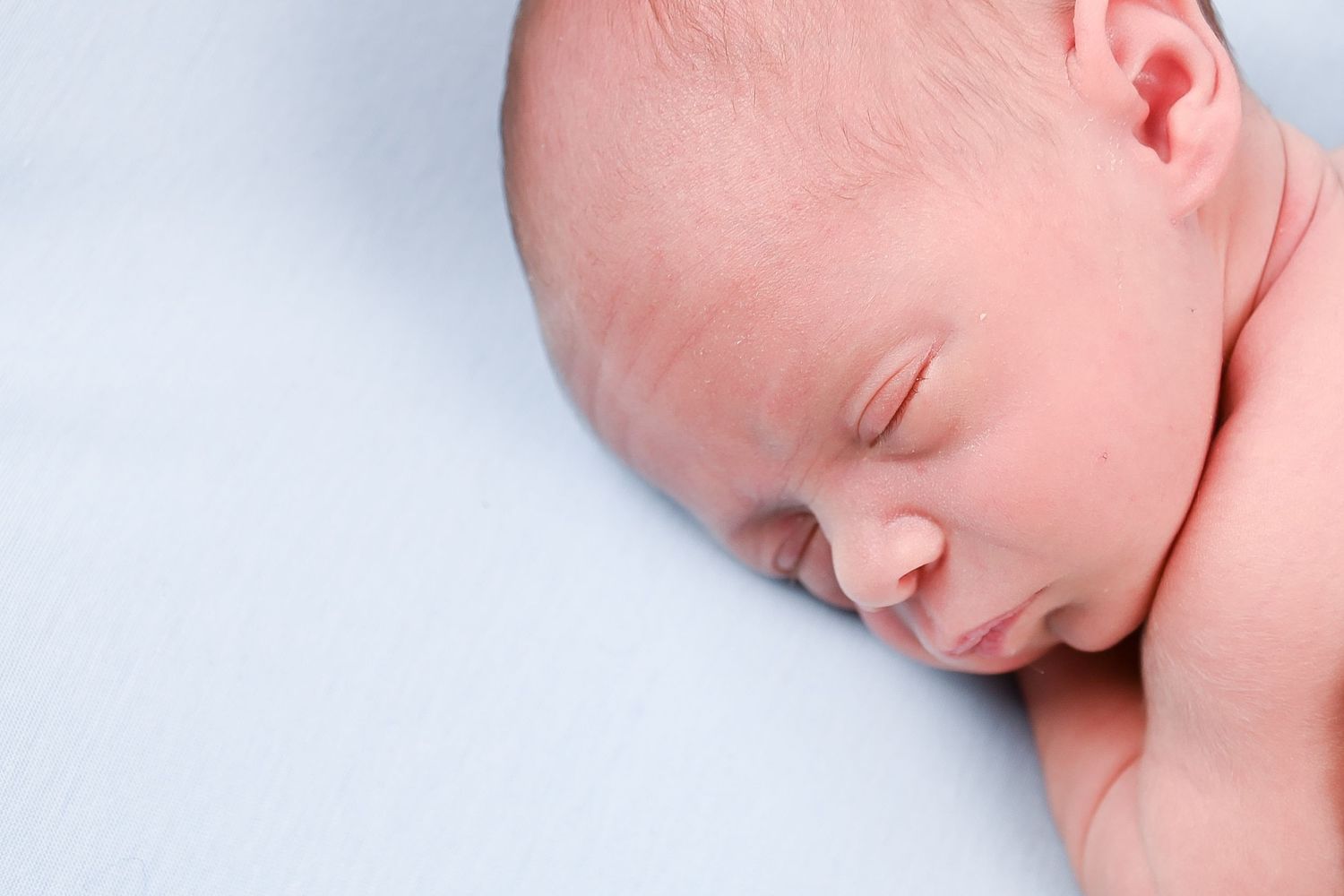 Close-up newborn baby portrait against soft blue background showing peaceful sleep.