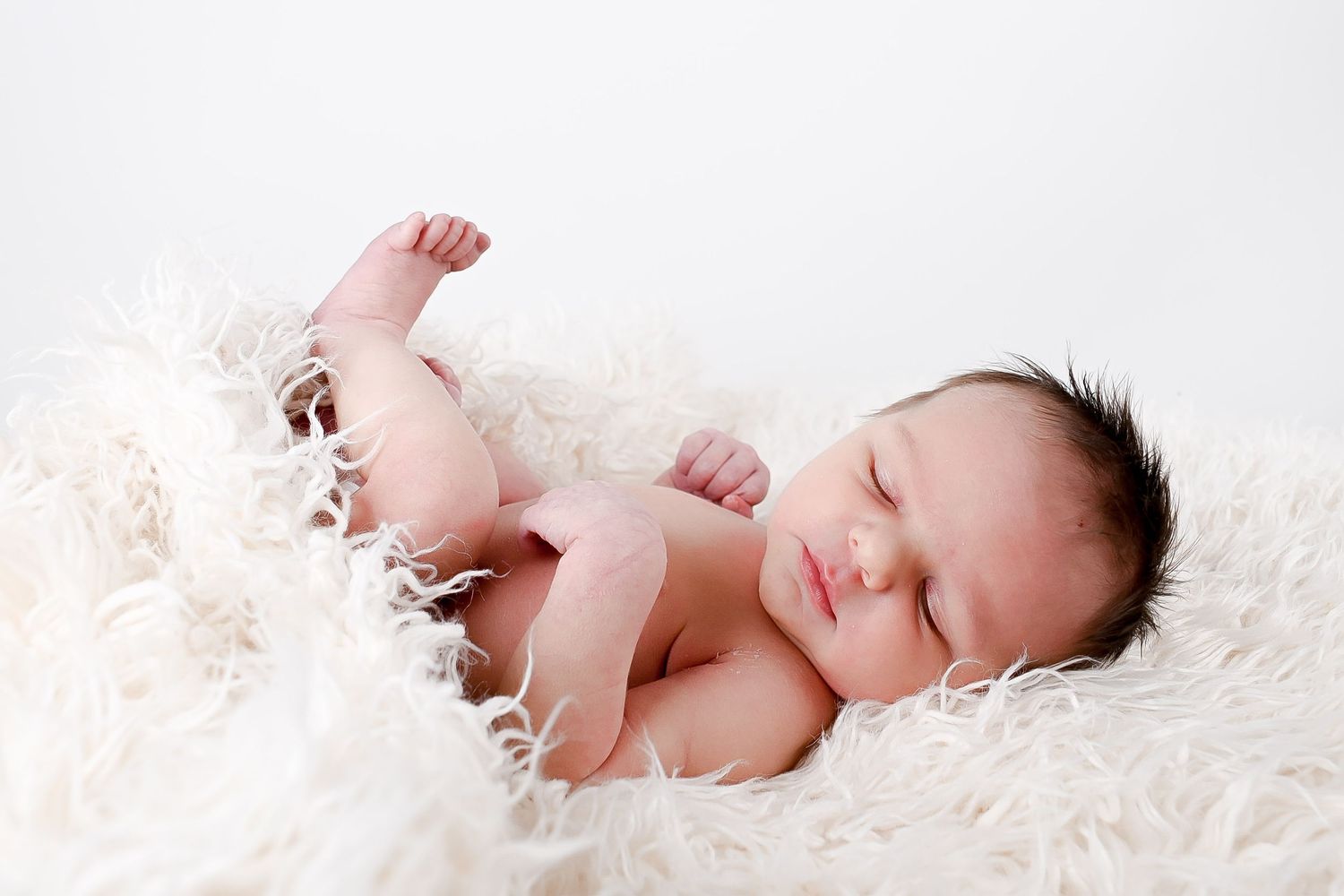 Newborn baby sleeping peacefully on soft white fluffy blanket in natural light.