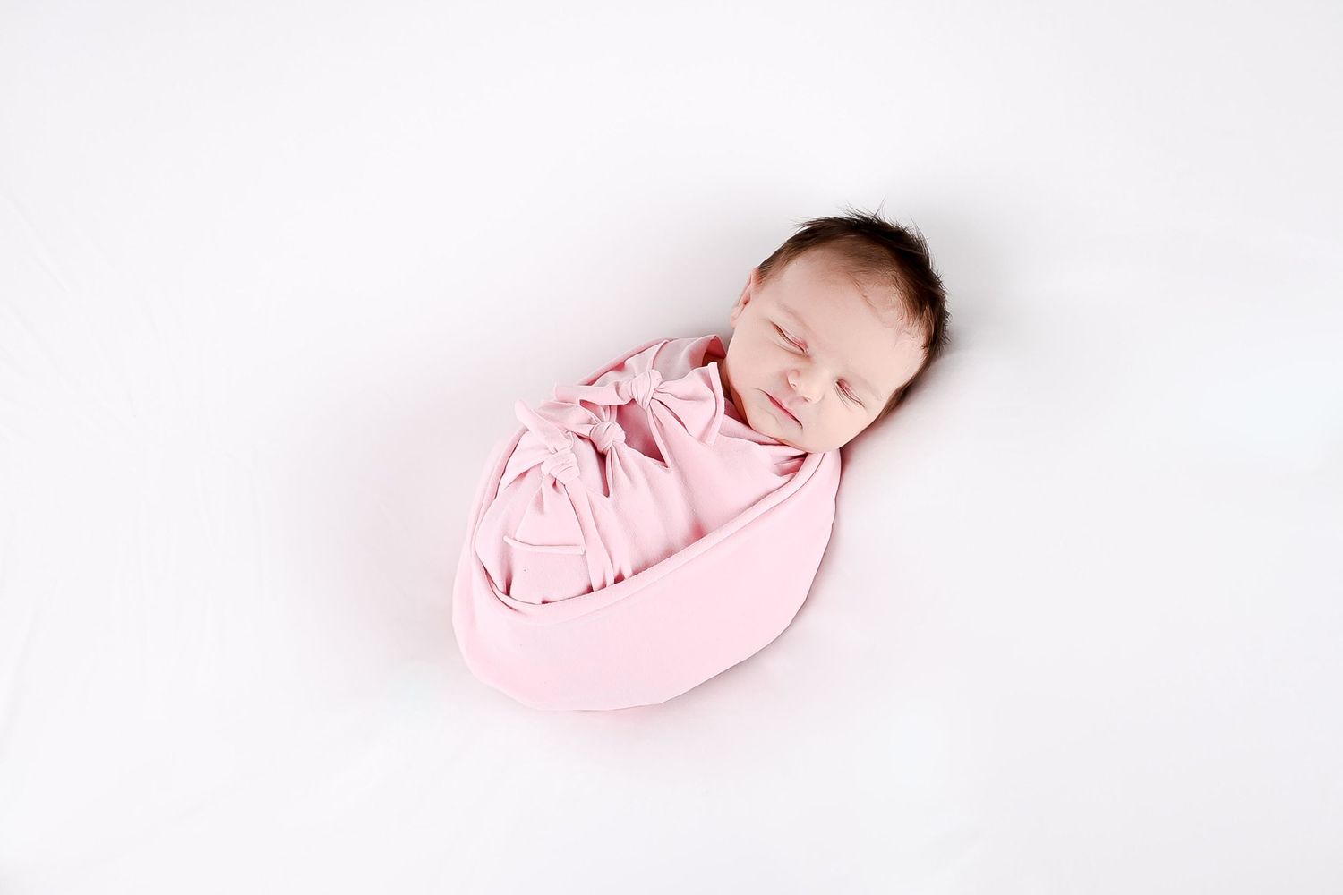 Sweet newborn baby wrapped in pink swaddle against white background.