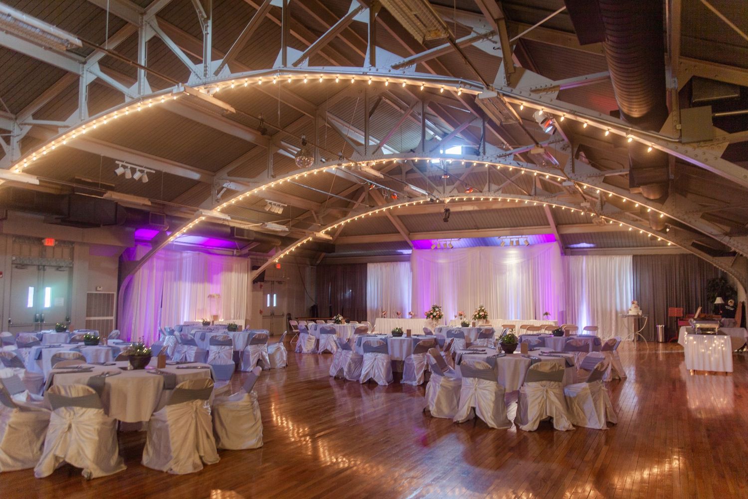 Wedding reception venue with string lights and purple uplighting creating a romantic atmosphere.