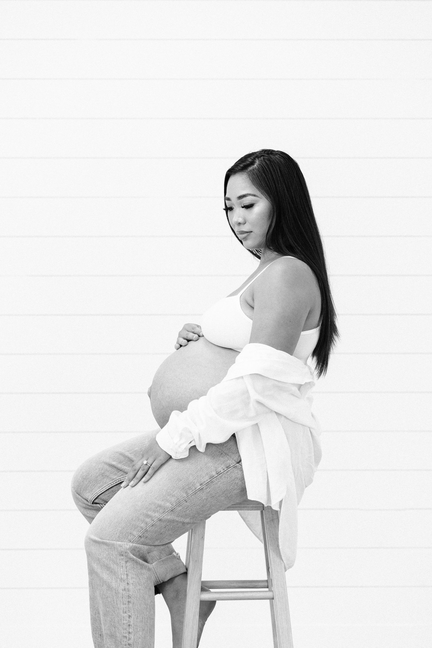 Black and white maternity portrait of an expectant mother in jeans and white top.