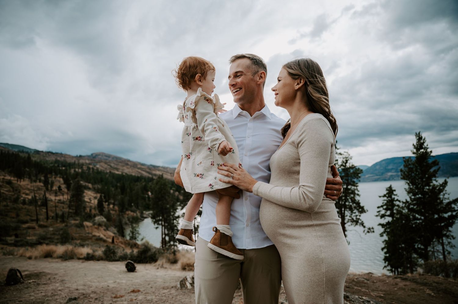 A family shares an intimate moment while standing on a cliff overlooking a scenic mountain lake.