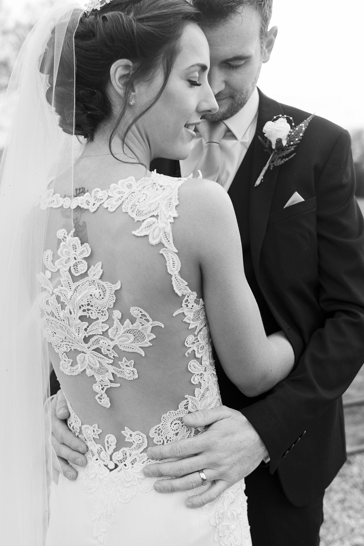 groom poses holding his brides waist as she wears a beautiful lace dress by Faye Amare Photography