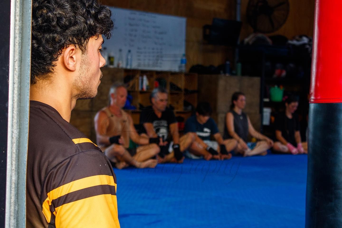 Martial arts students sitting on blue mats in boxing gym during training session.