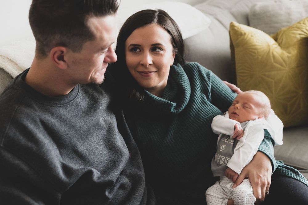 a new set of parents sitting on the couch holding their newborn son