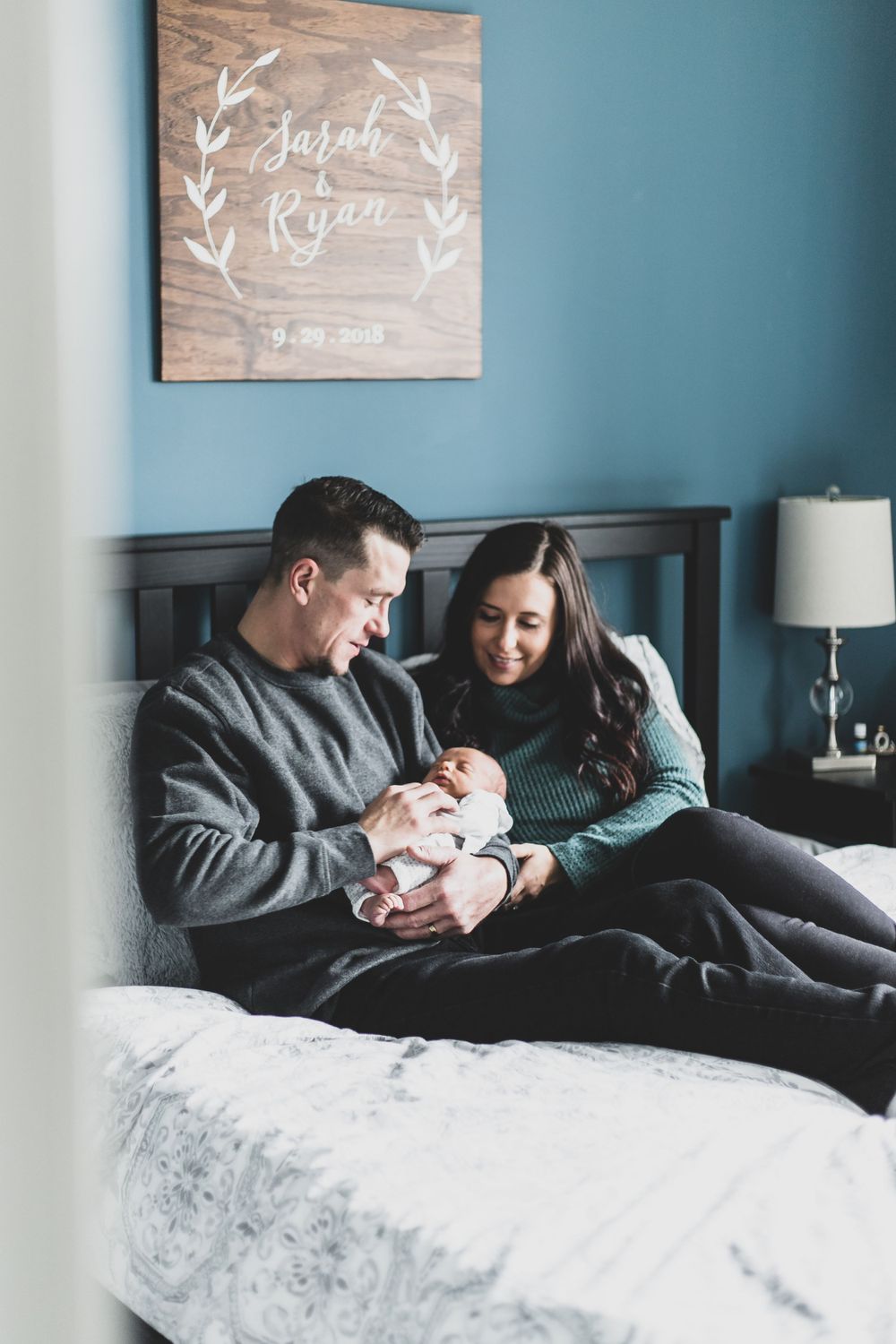 peeking into a bedroom with new parents sitting on their bed admiring their son