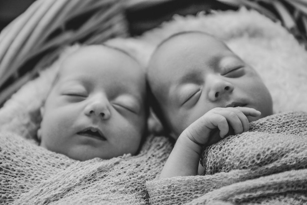 twin newborns wrapped up and placed in a blanket while sleeping