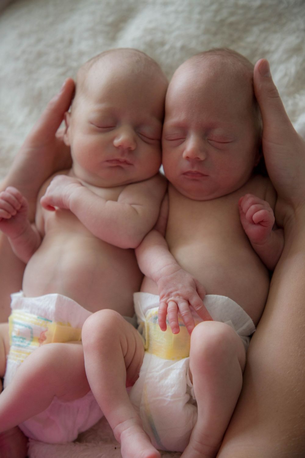 a mother holding her newborn twin daughters side by side while they sleep