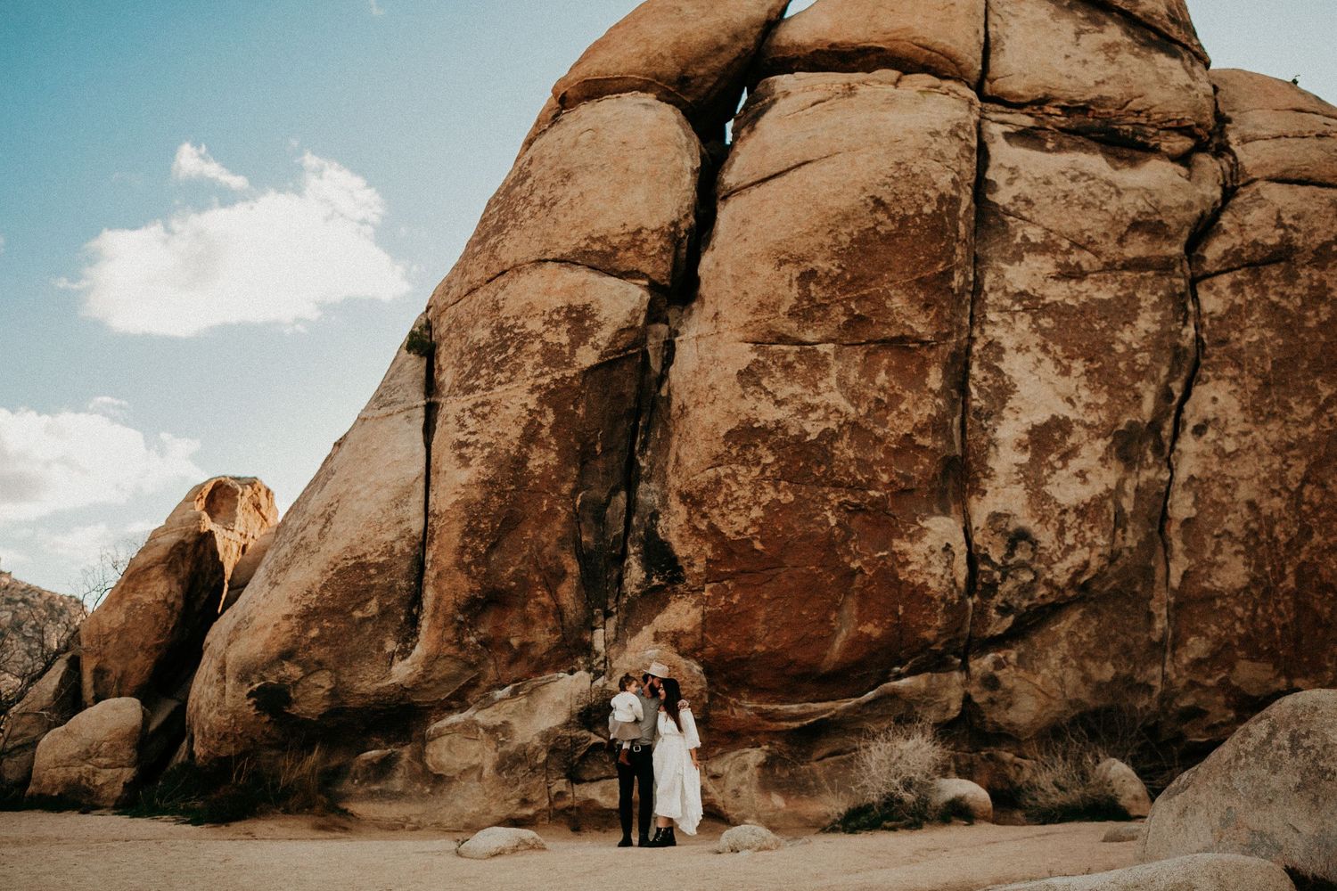 Couple embraces against massive desert rock formation under blue sky.