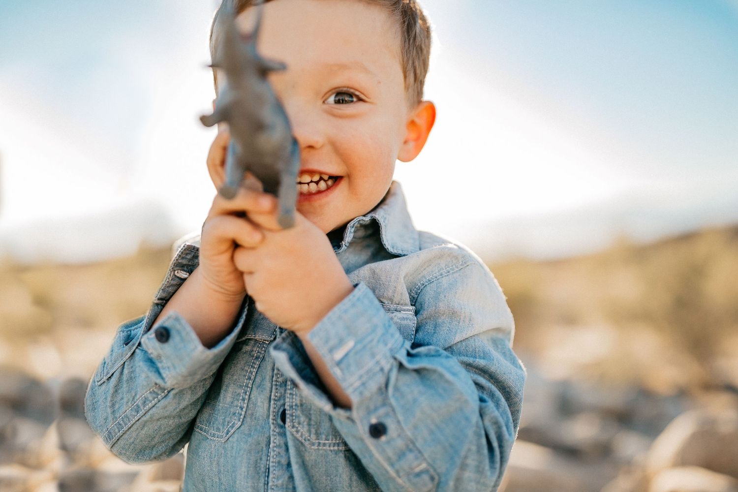 Child in denim jacket plays with toy in warm desert sunlight.