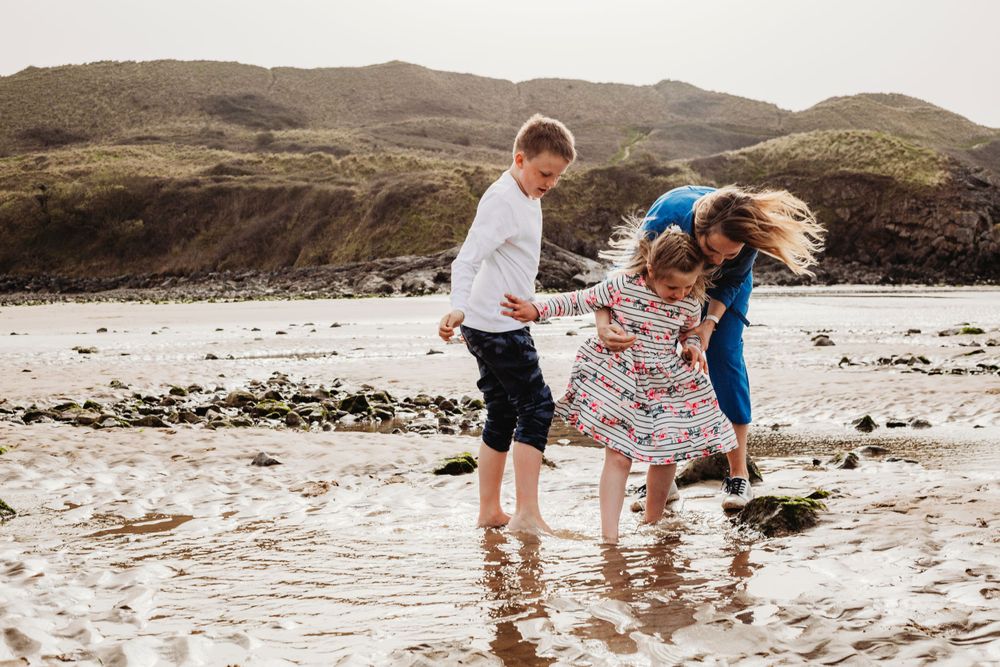 Children playing and splashing in shallow ocean water near rocky coastline.