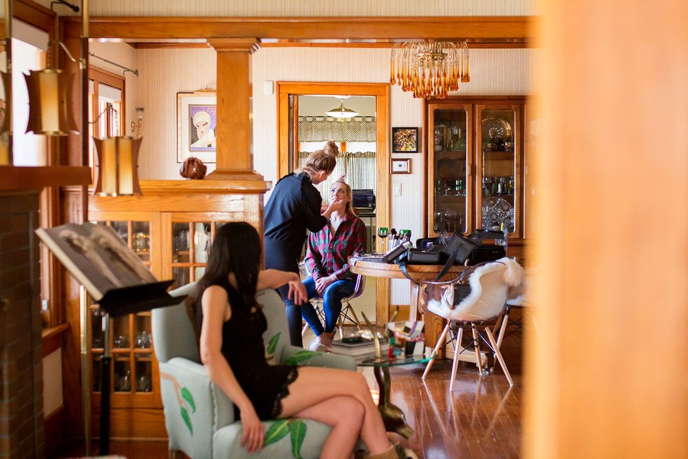 Stylists prepare for a special event in a warmly lit room with wooden beams and decorative lighting.