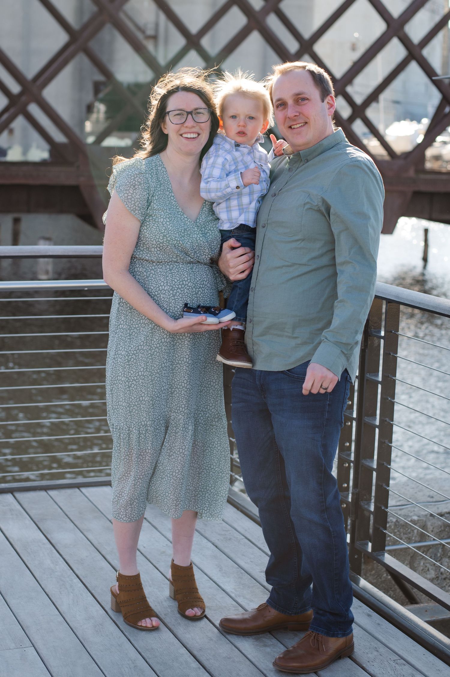 Family portrait on wooden boardwalk with metal industrial structure in background.