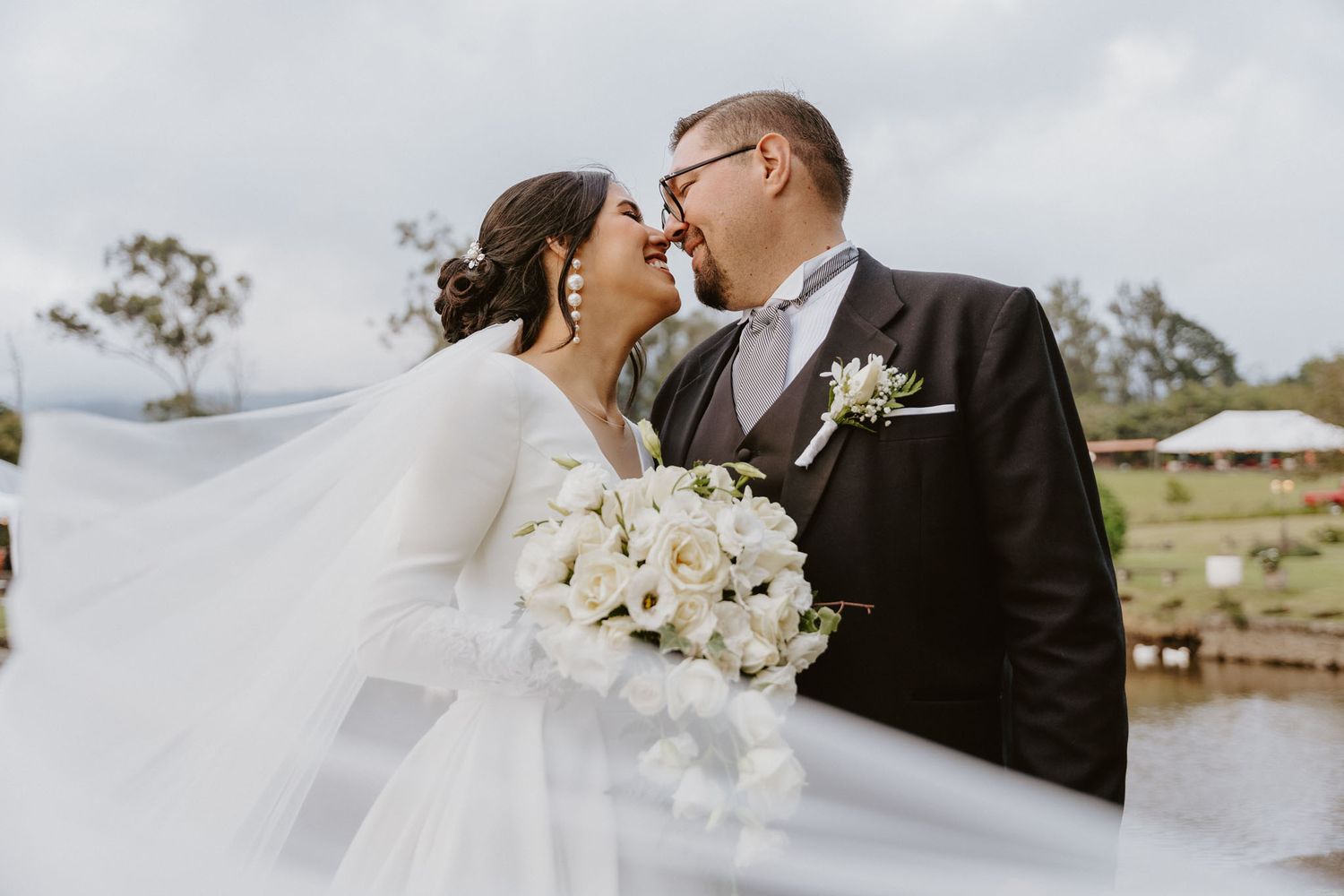 Romantic wedding moment with white bouquet and flowing veil against cloudy sky, boda, heredia, costa rica, wedding photography, novios