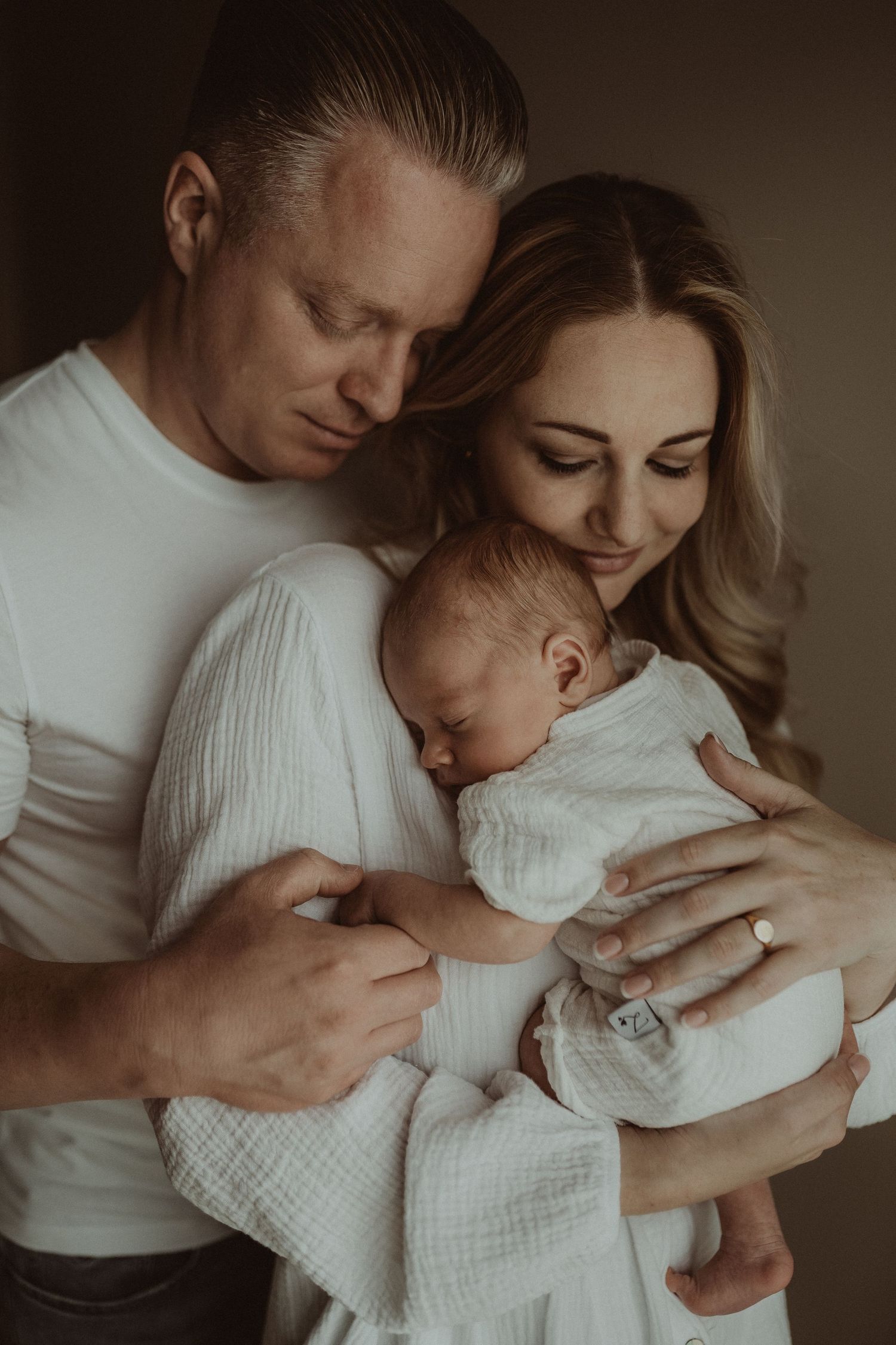 Intimate family portrait in white clothing with soft moody lighting.
