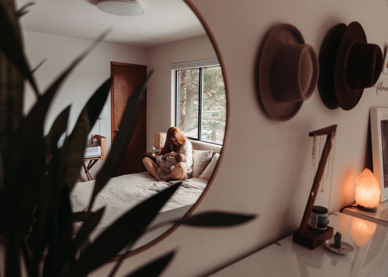 Reflection in round mirror showing cozy room interior with hats on wall and warm lighting.