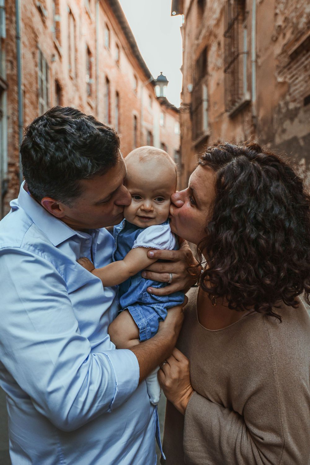 An intimate family portrait showing loving kisses shared with a smiling baby in a historic street.