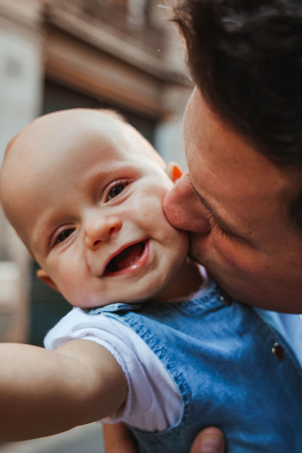 A joyful close-up moment of affection with a laughing baby in blue clothing.
