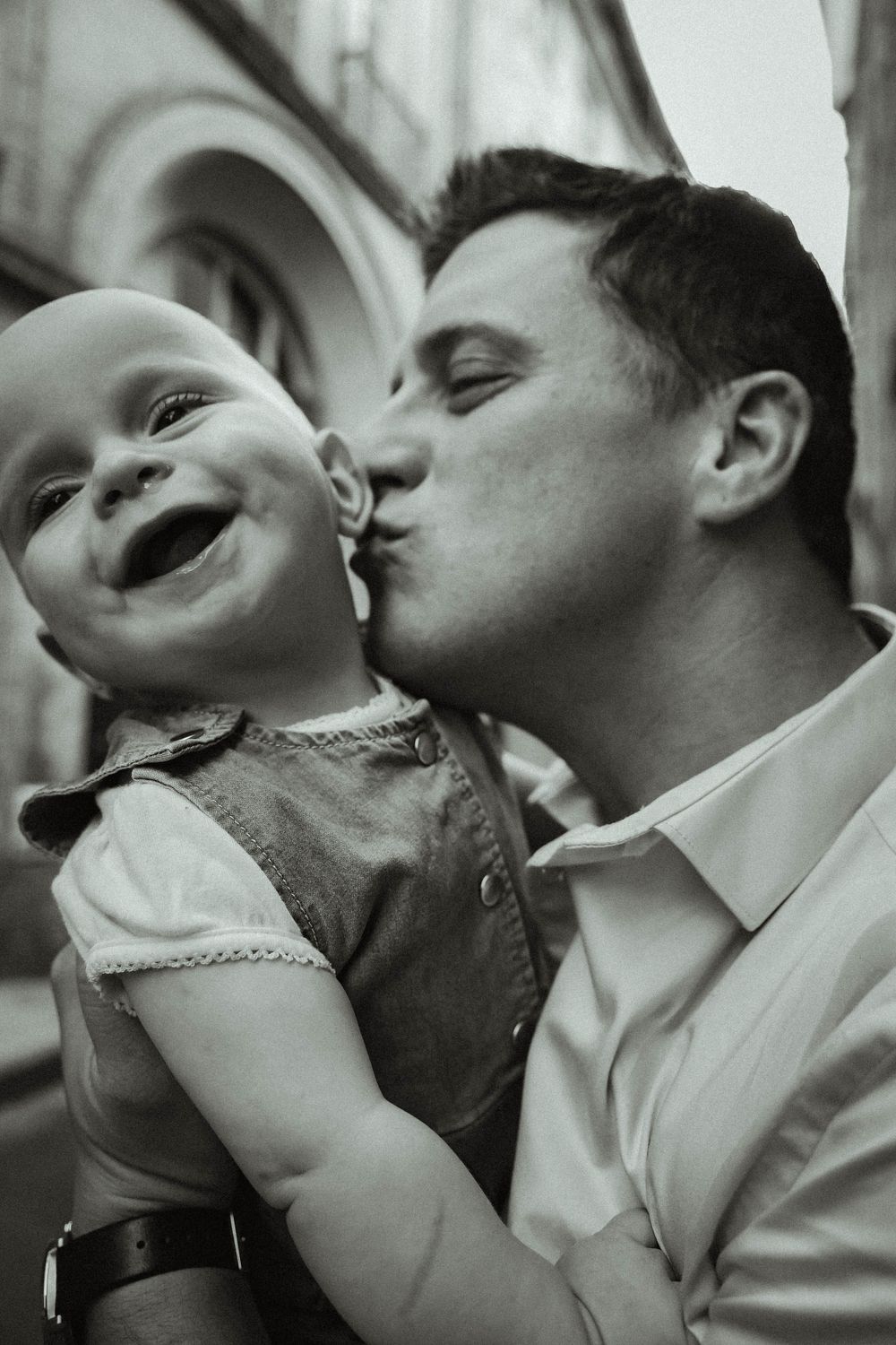 A black and white portrait capturing a sweet moment of laughter and kisses.