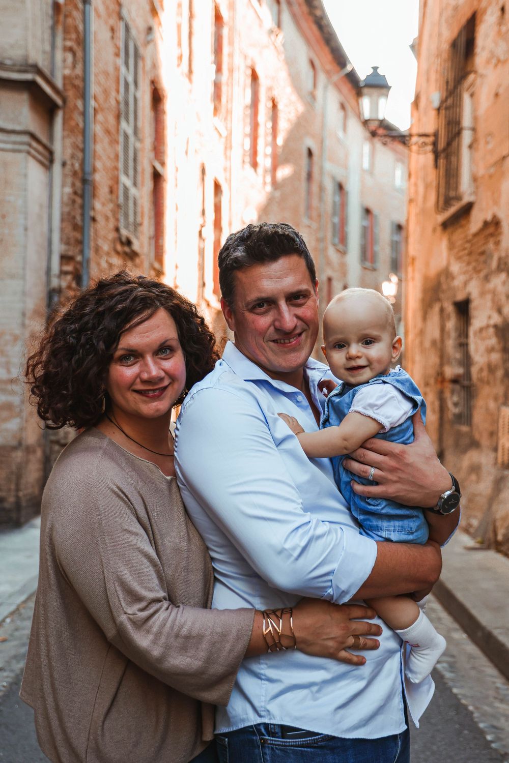 A family poses together in a charming European alleyway with rustic stone walls.