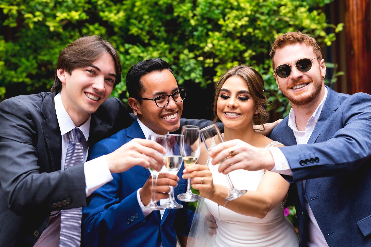 Wedding party toasting with champagne glasses in an outdoor garden setting.