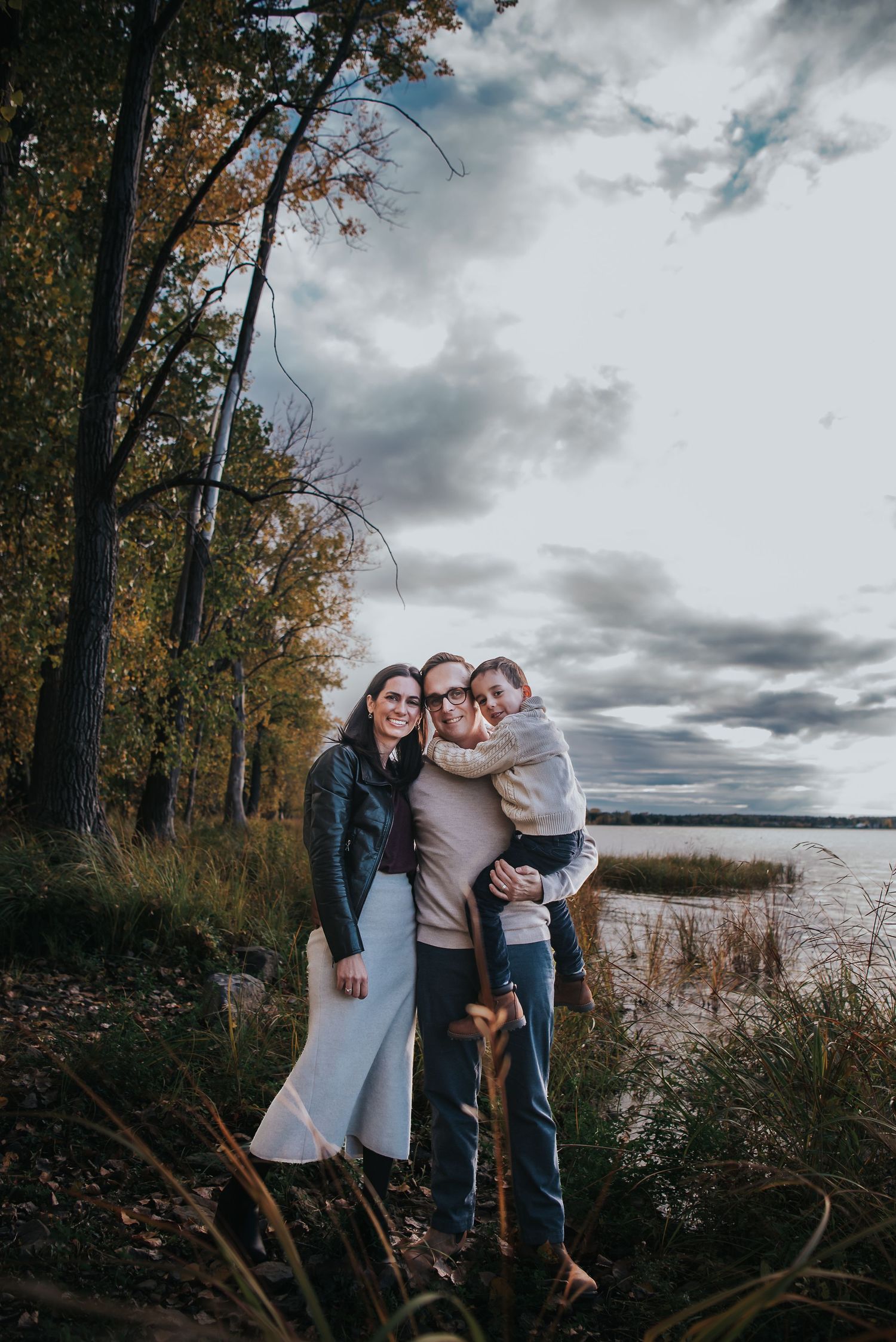 Beautiful family of three holds one another with cloudy sky behind them.
