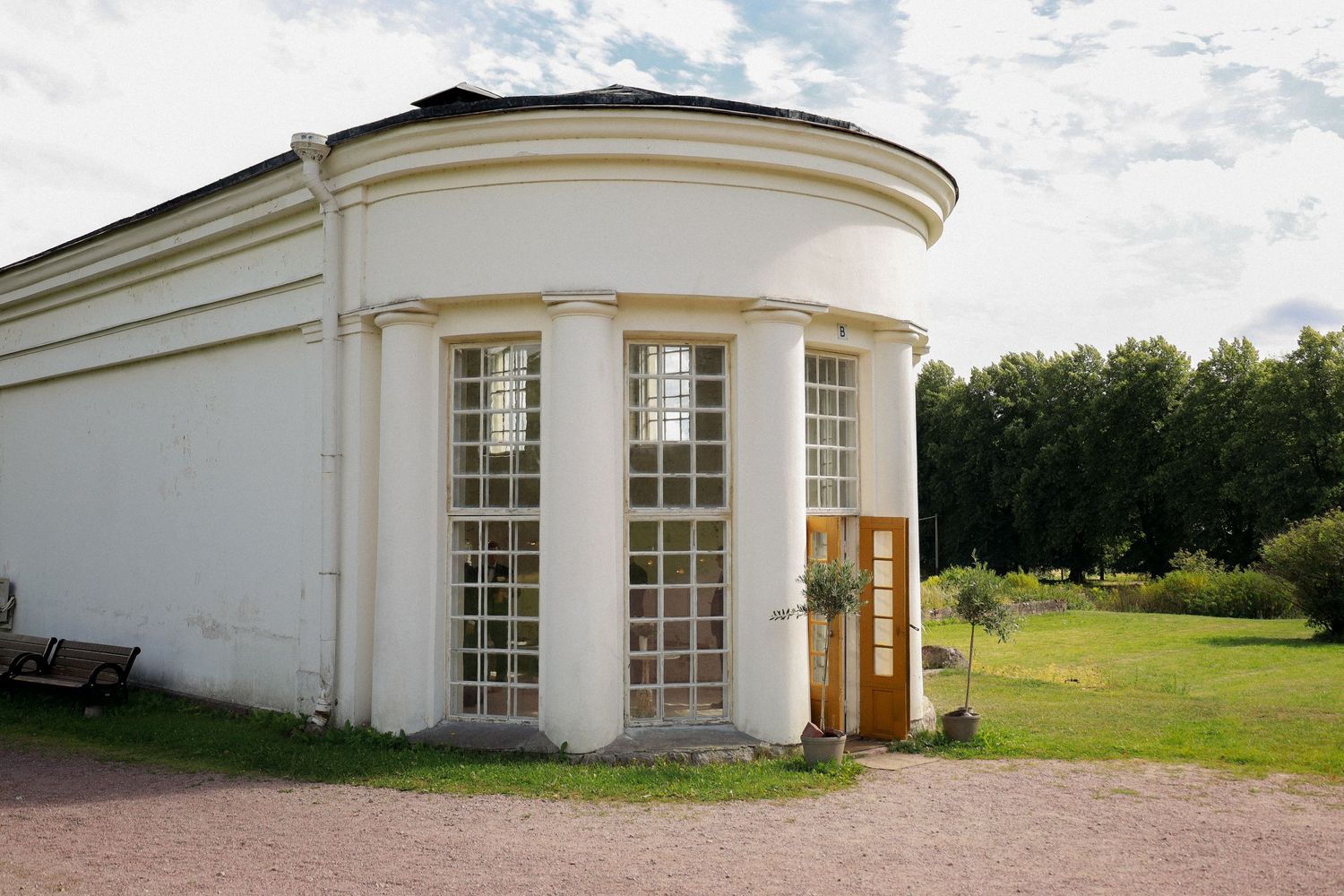 White curved architectural building with tall windows and a rounded facade in a garden setting.