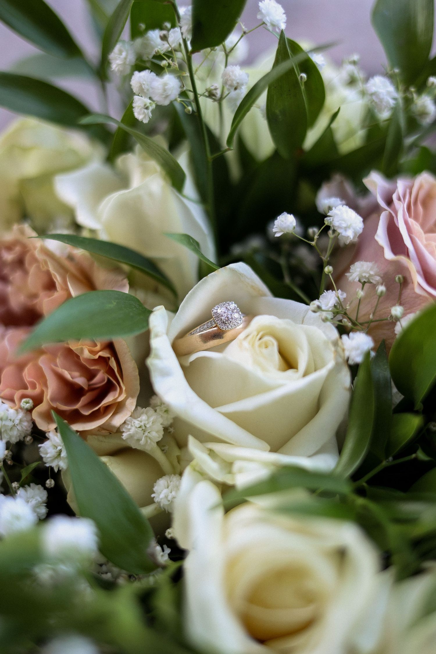 Close-up of cream and blush roses with baby's breath flowers and a diamond engagement ring nestled in petals.