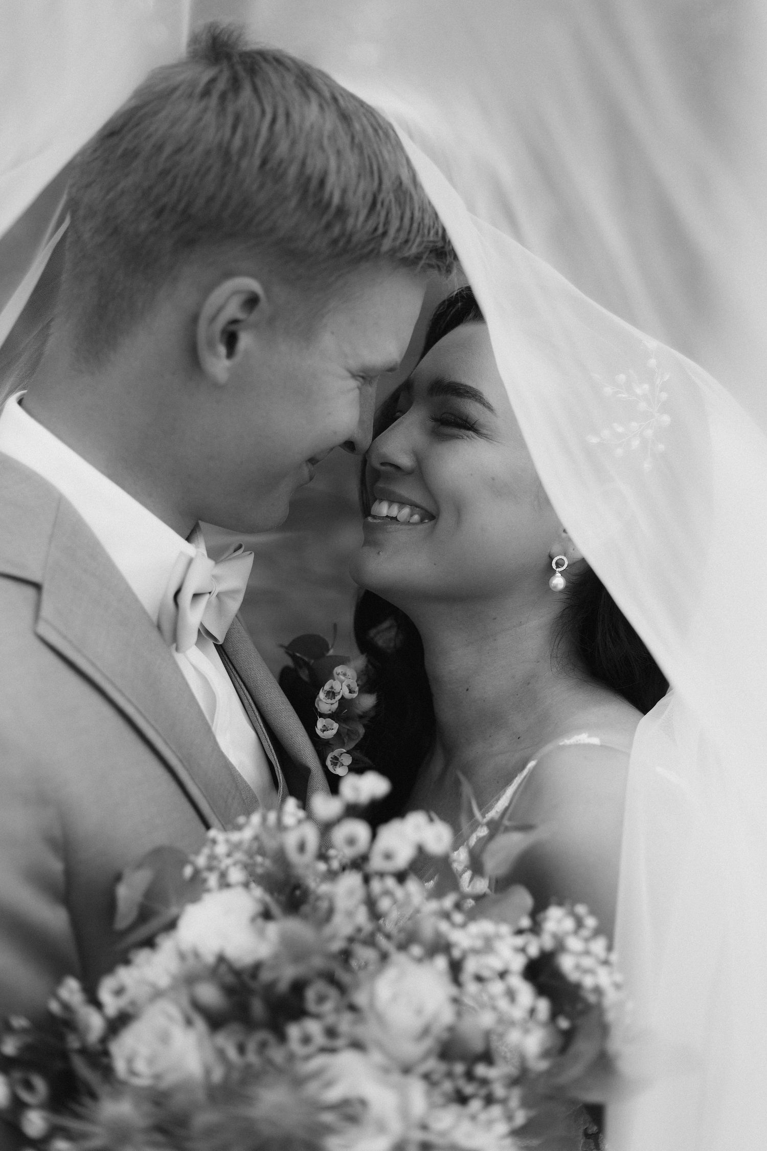 Intimate black and white portrait of newlyweds sharing tender moment under veil.