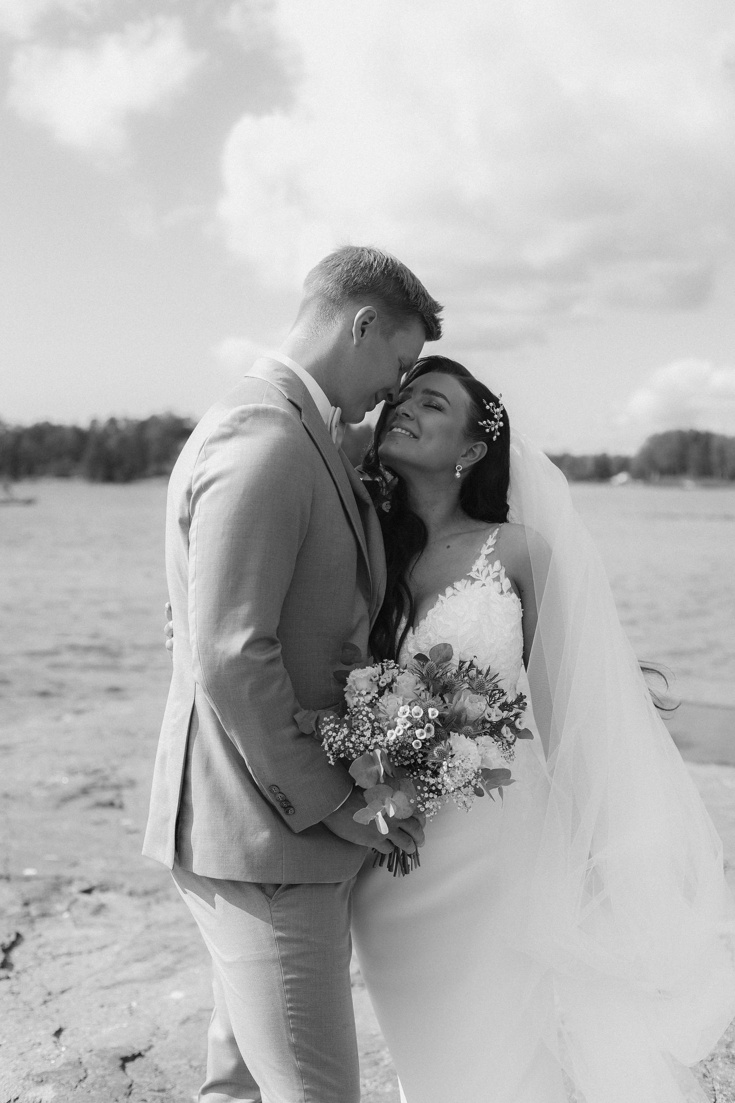 A black and white beach wedding photo showing a tender moment between newlyweds.