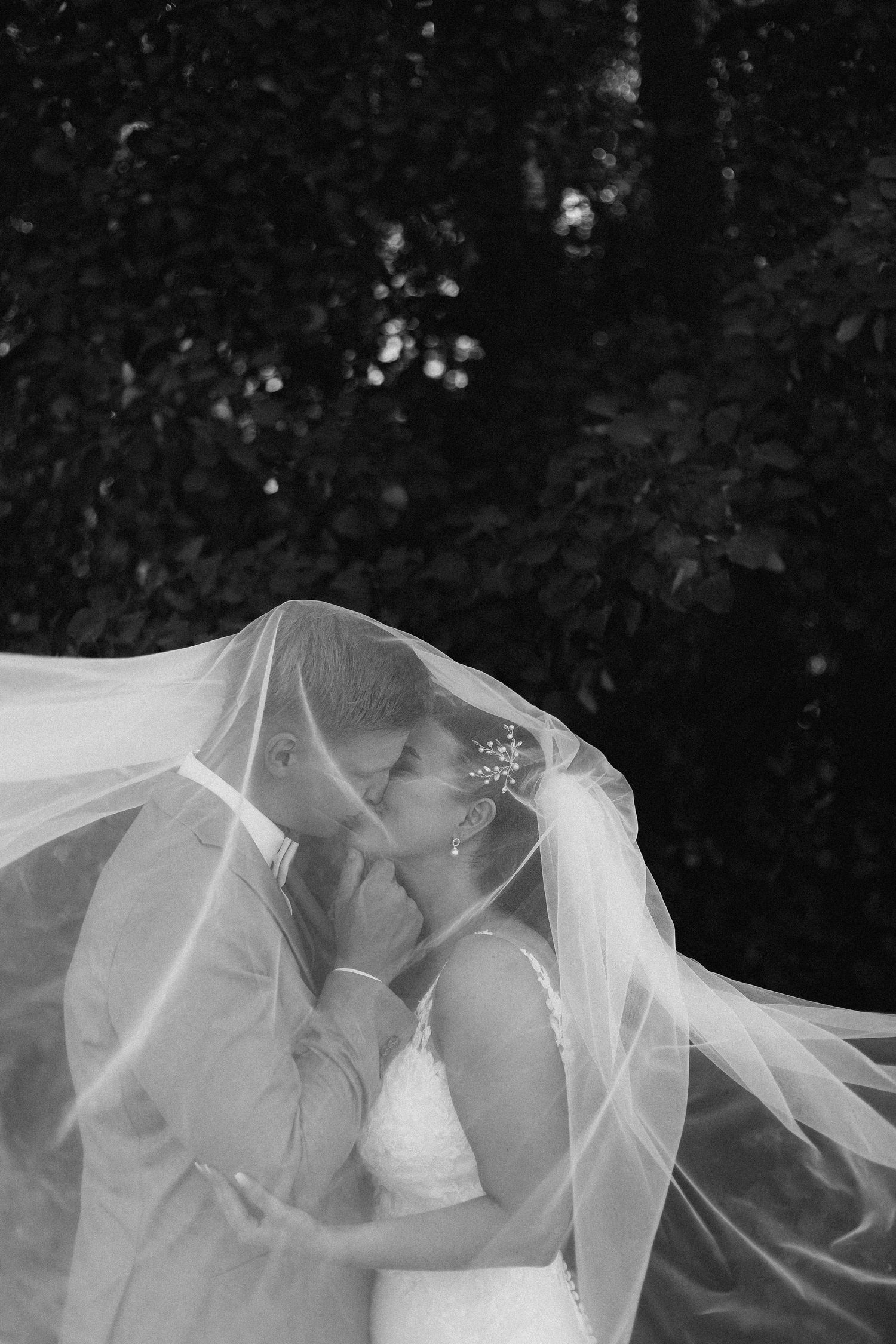 A dramatic black and white wedding photo under flowing veil capturing an intimate moment.