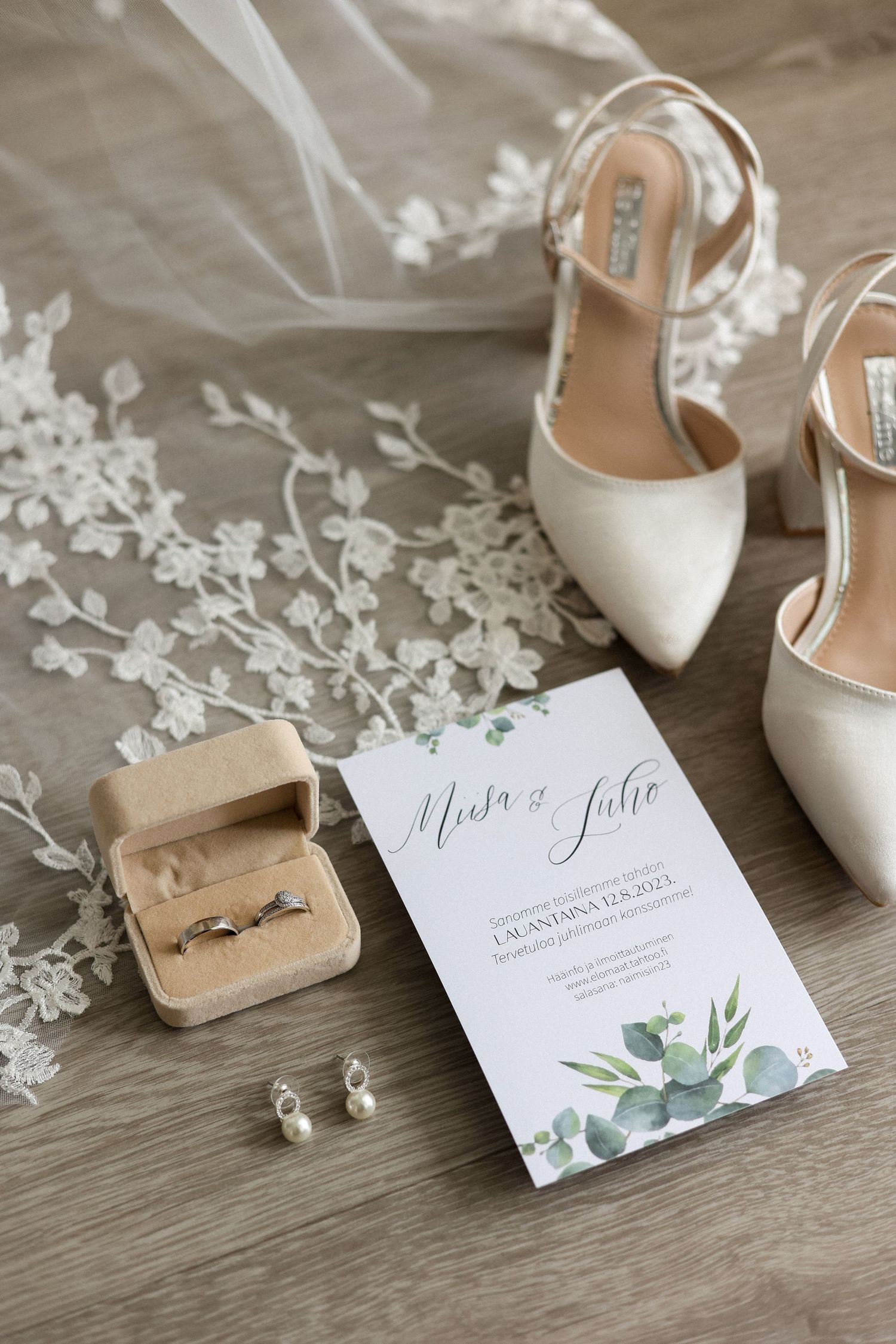 Wedding details flatlay with white heels, invitation card and floral lace accents.