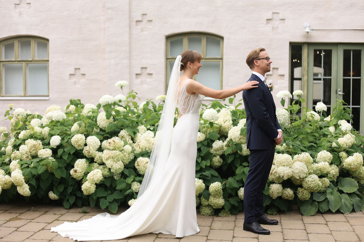 A bride and groom pose playfully by blooming hydrangea bushes.