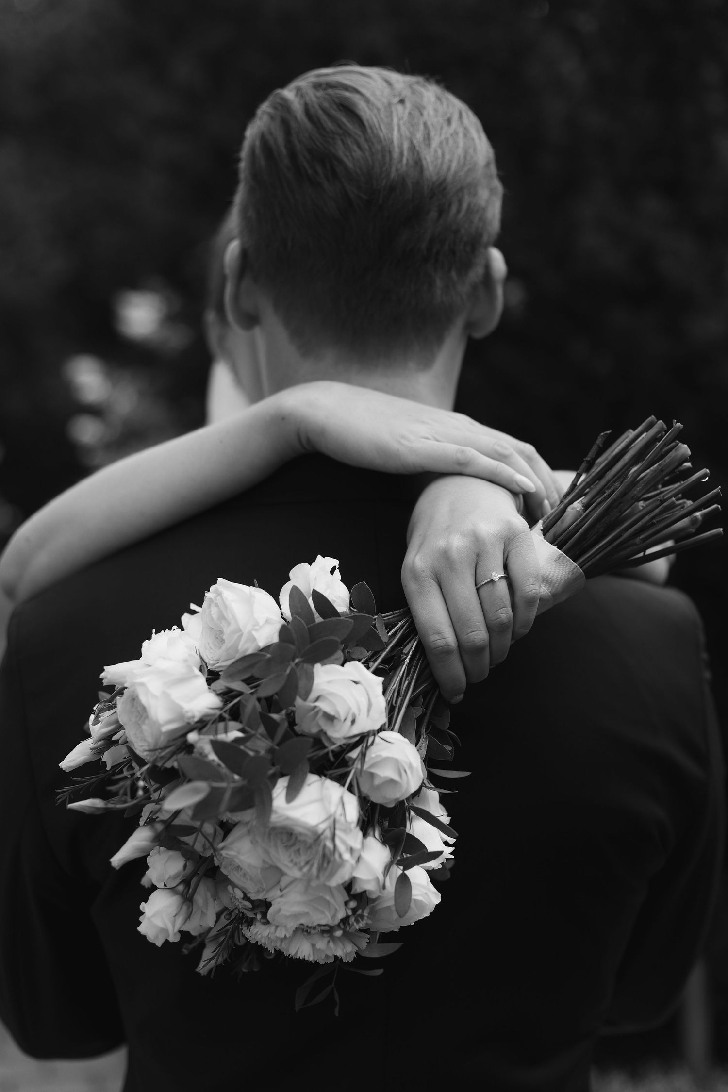 Black and white photo of an embrace with white roses visible.