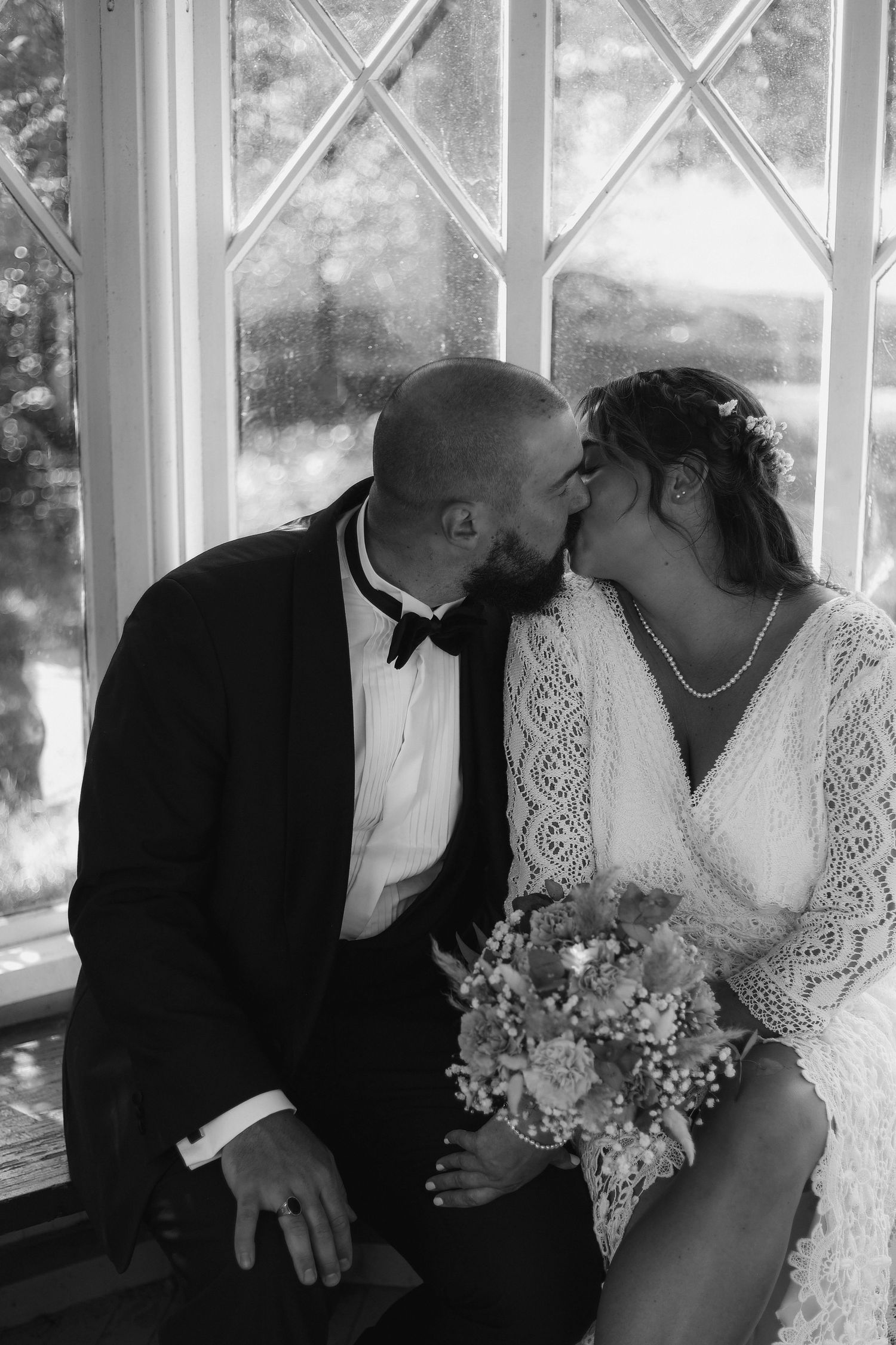 Intimate black and white wedding portrait by window with romantic natural lighting.