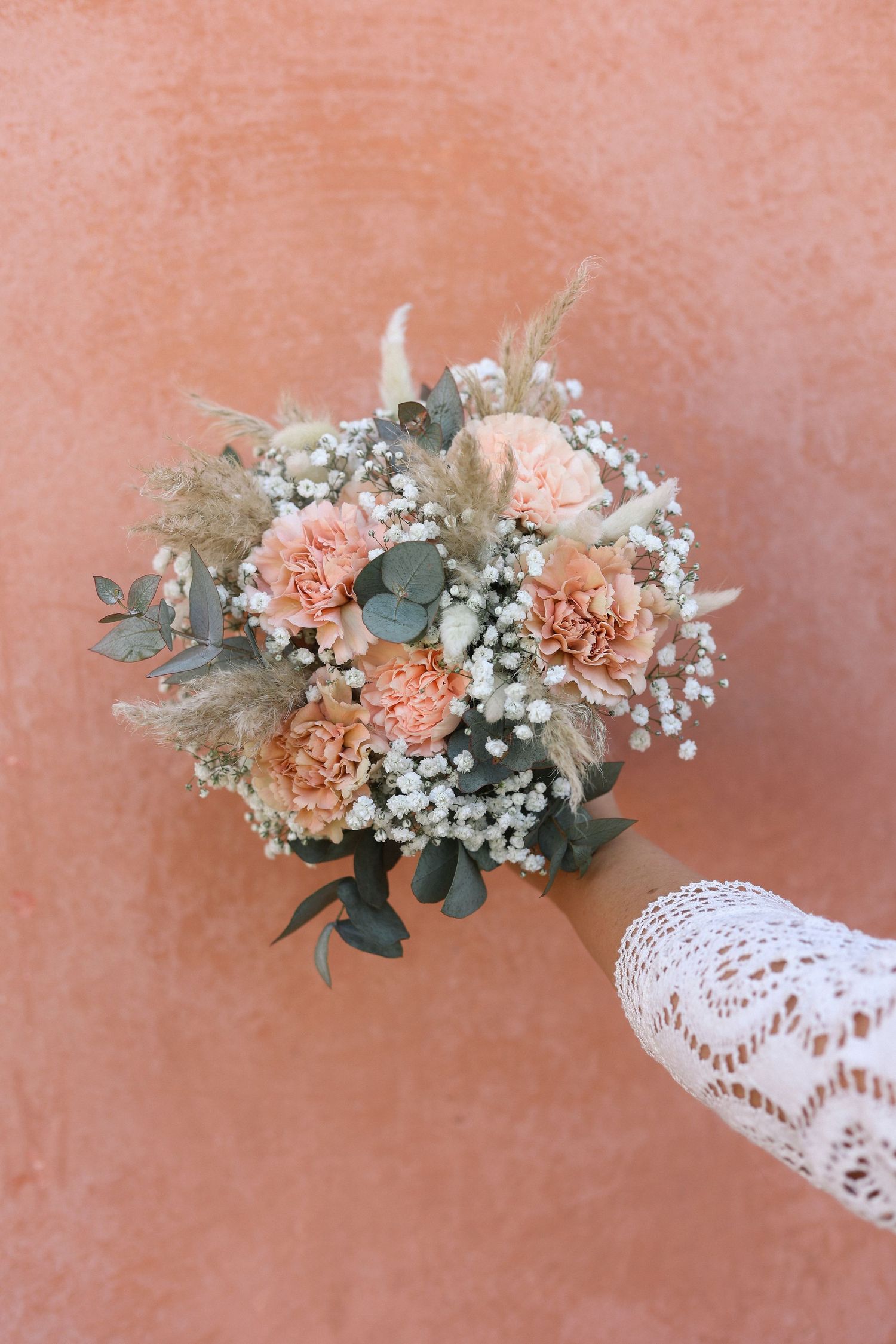 Delicate bridal bouquet with peach carnations and baby's breath against coral background.