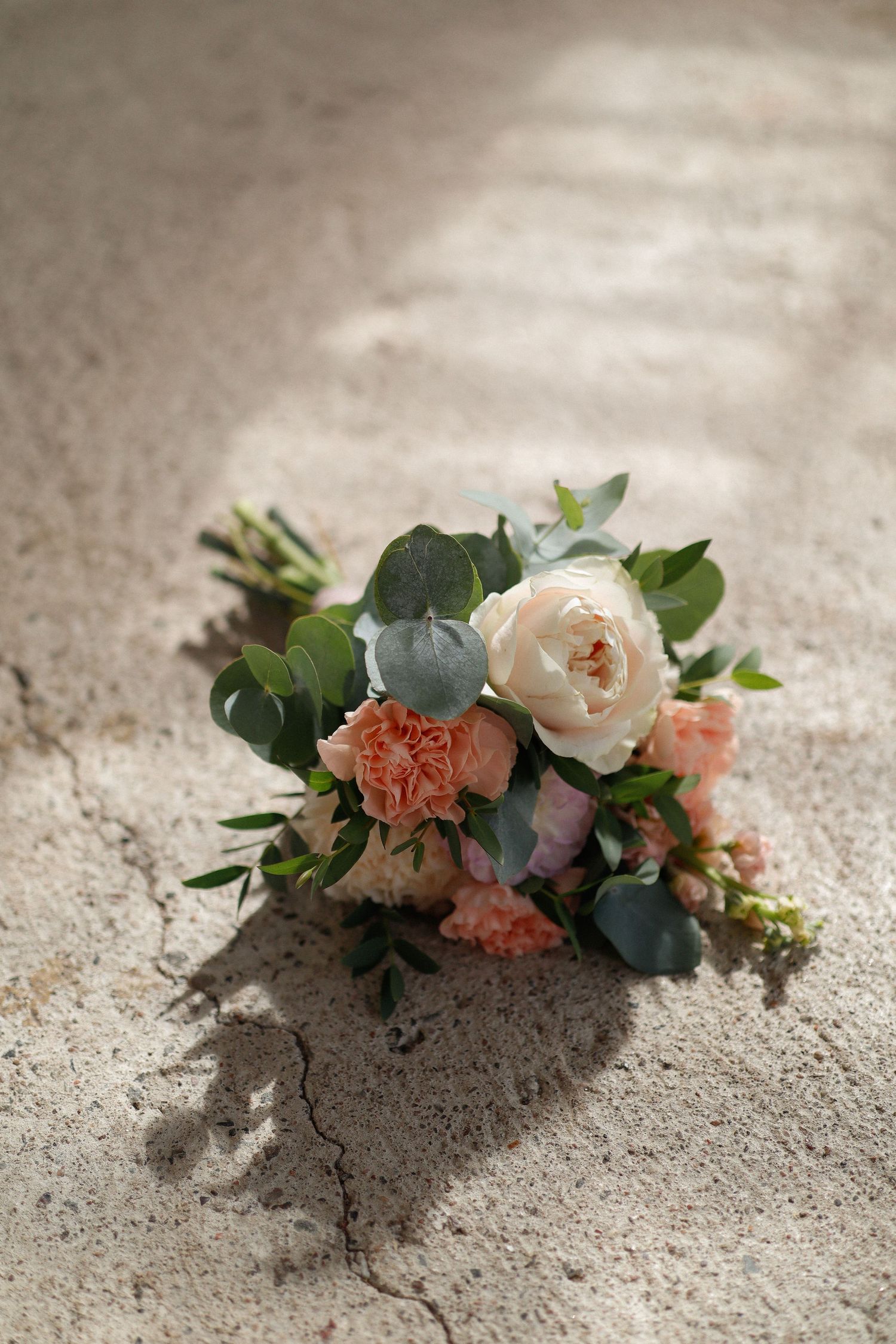 Delicate bridal bouquet with roses and eucalyptus on concrete.