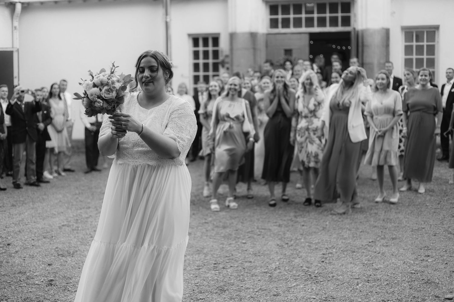 Black and white photo of wedding bouquet toss with excited guests.