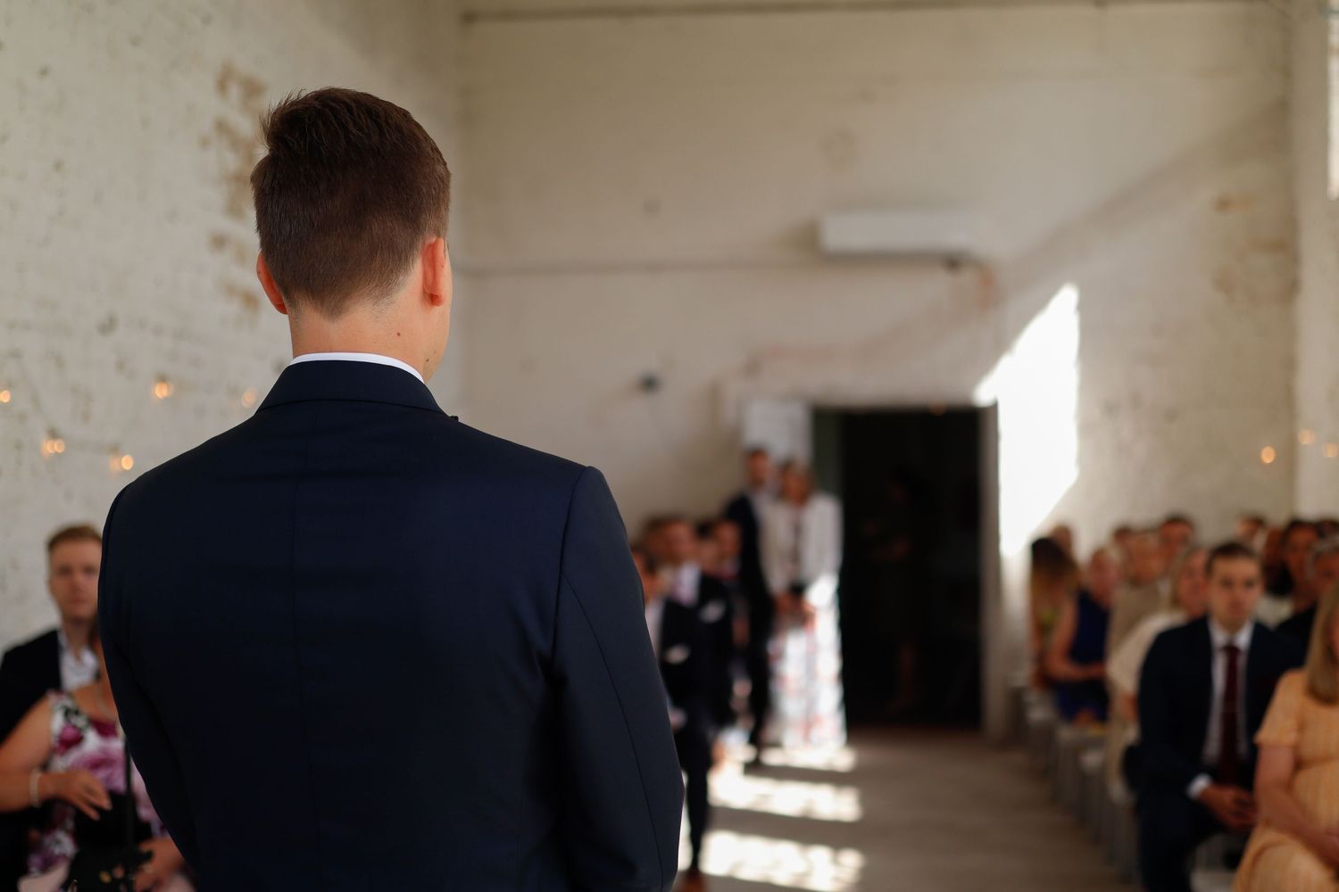 Wedding ceremony scene with guests seated in rows at an indoor venue with natural lighting.