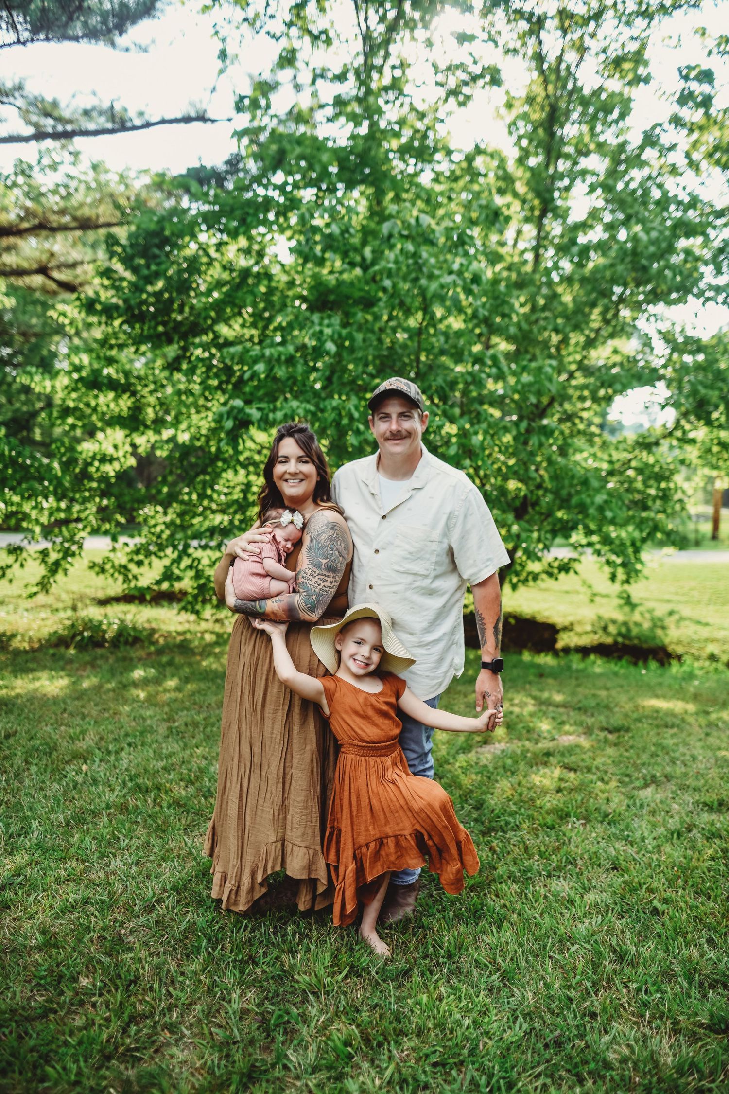 Family wearing brown and rust colored outfits poses together on grassy hill during outdoor photo session.