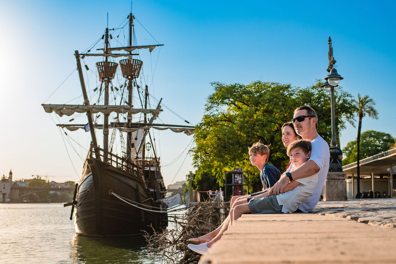 Historic wooden sailing ship replica docked at sunset against blue sky.